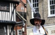 A man in Civil War costume holds a pike over his arm in front of some timber-framed Newark buildings